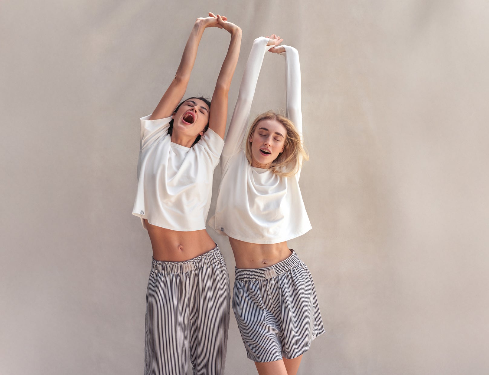 Two people wearing white t-shirts and gray shorts against a plain background