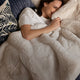 Woman lying on a bed under a fluffy white Sunday Citizen Faux Fur Bed Runner