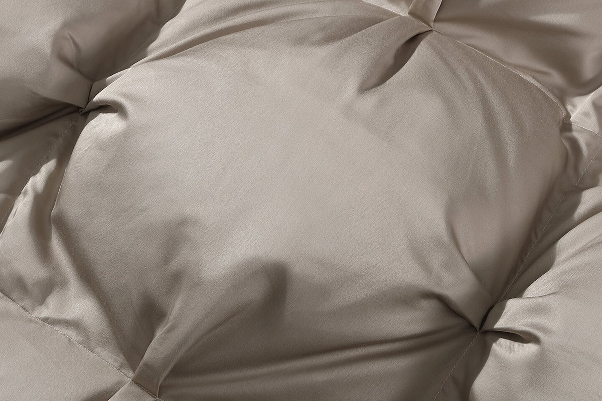 A close-up of a light taupe or beige quilted duvet or comforter, showing the soft texture and stitched channels.