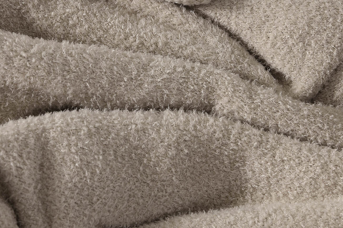 A close-up of a soft, plush fleece or sherpa fabric in a warm taupe-beige color, showing the textured pile and draped folds.