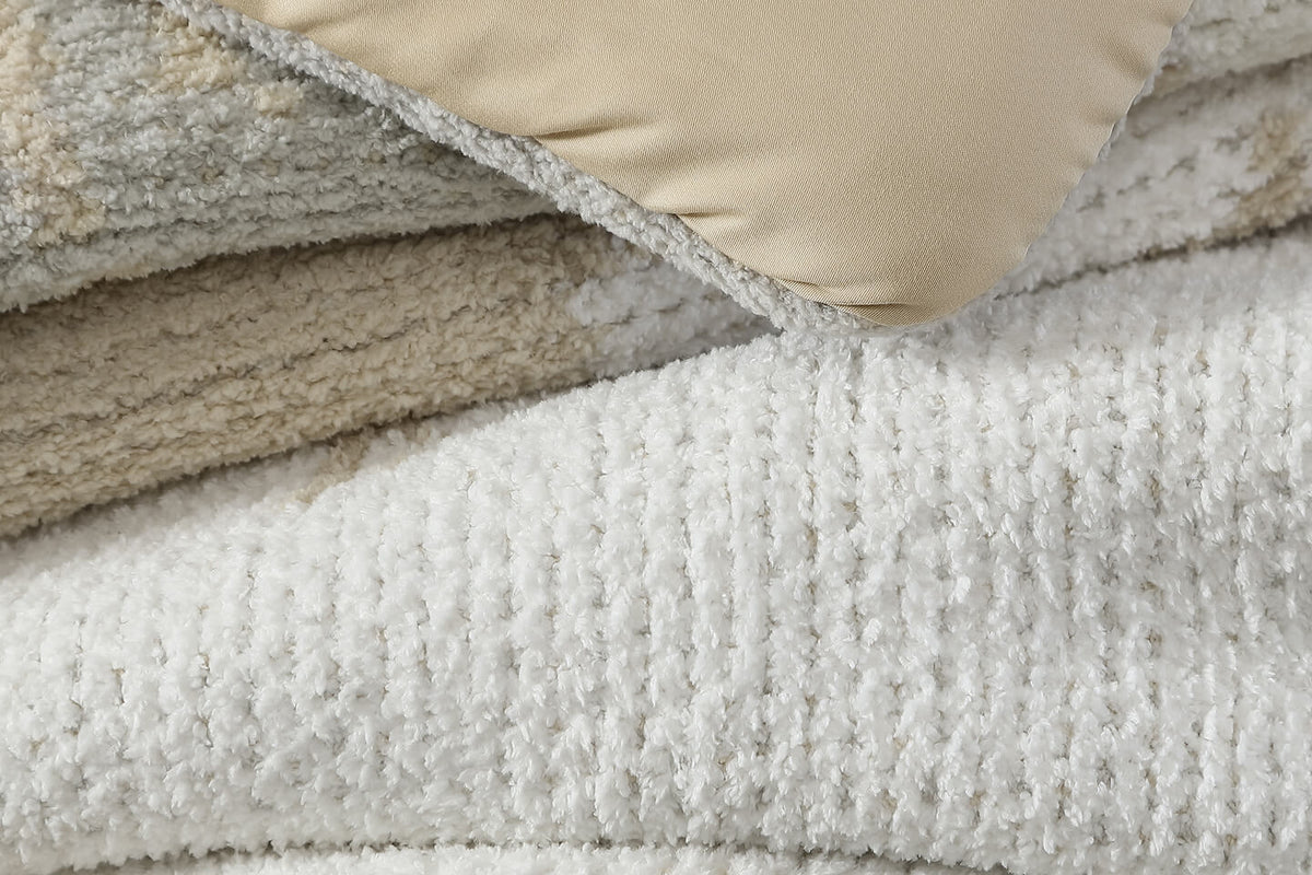 Close-up of a plush textured throw blanket in off-white, folded with a beige pillow or cushion partially visible at the top.