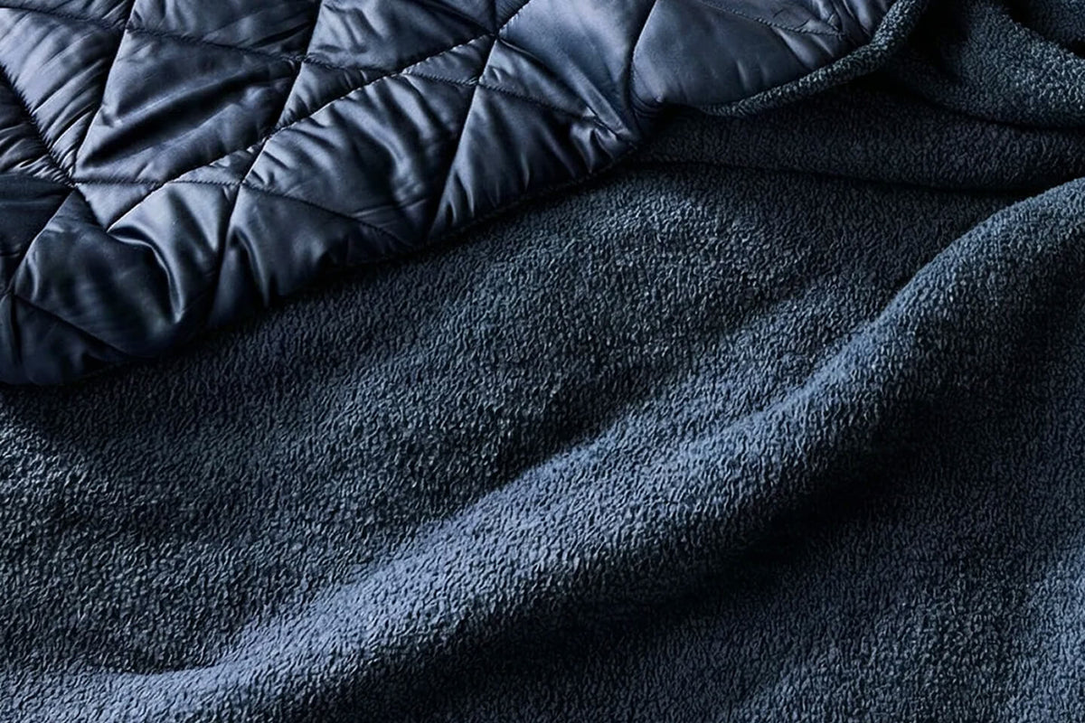 Close-up of a dark navy blue fleece blanket with a quilted puffer fabric section layered on top, showing the soft textured surface and stitched diamond pattern.