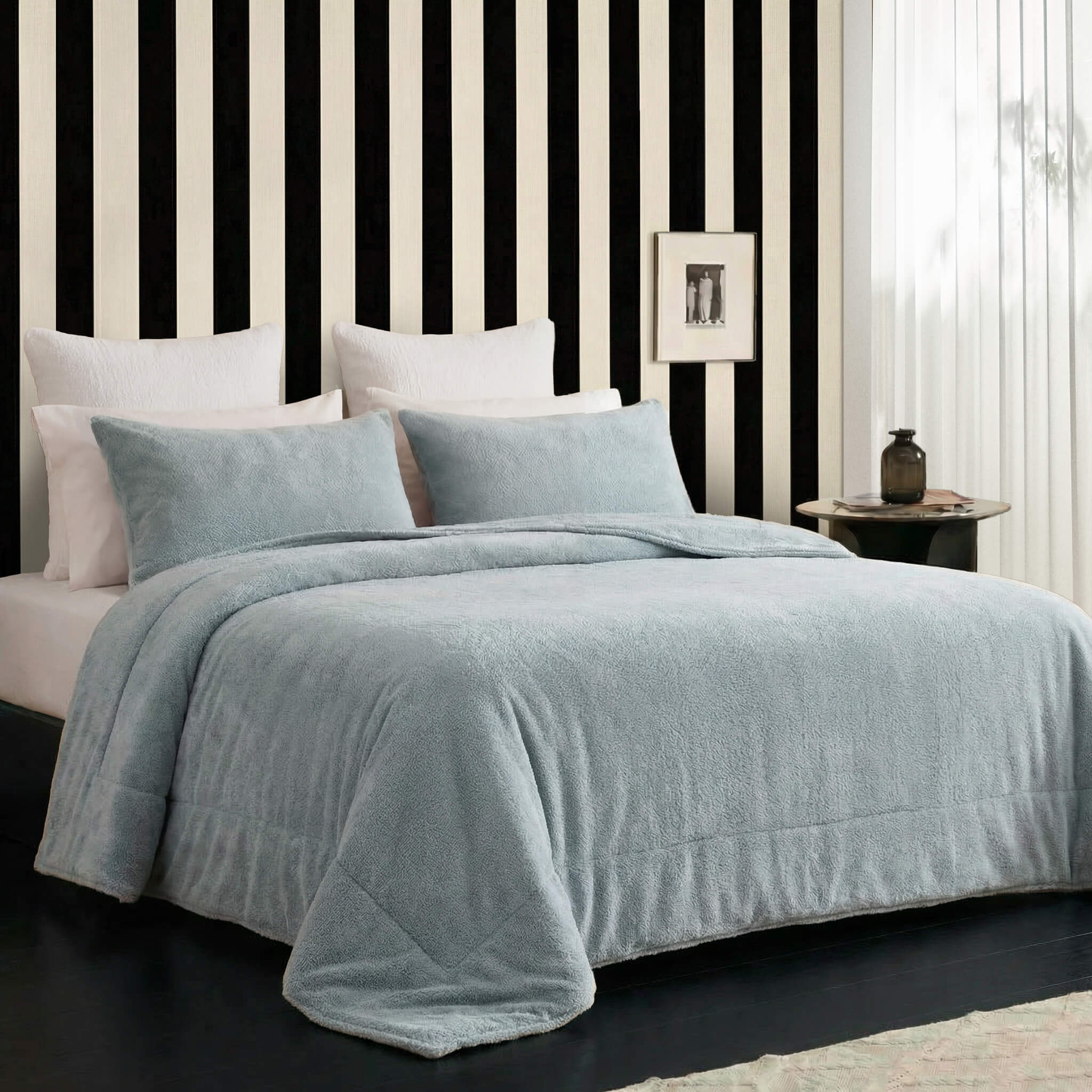 Sunday Citizen Snug Sham Set and Comforter in Misty Blue on a bed with striped wall and side table in the background